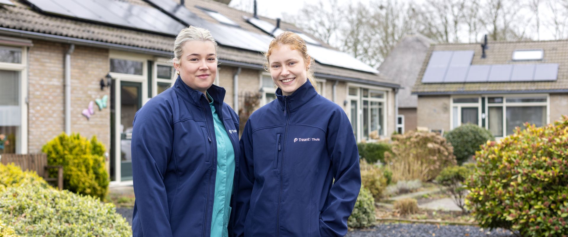 Twee personen in werkkleding van Treant Thuis staan buiten voor een woningen.