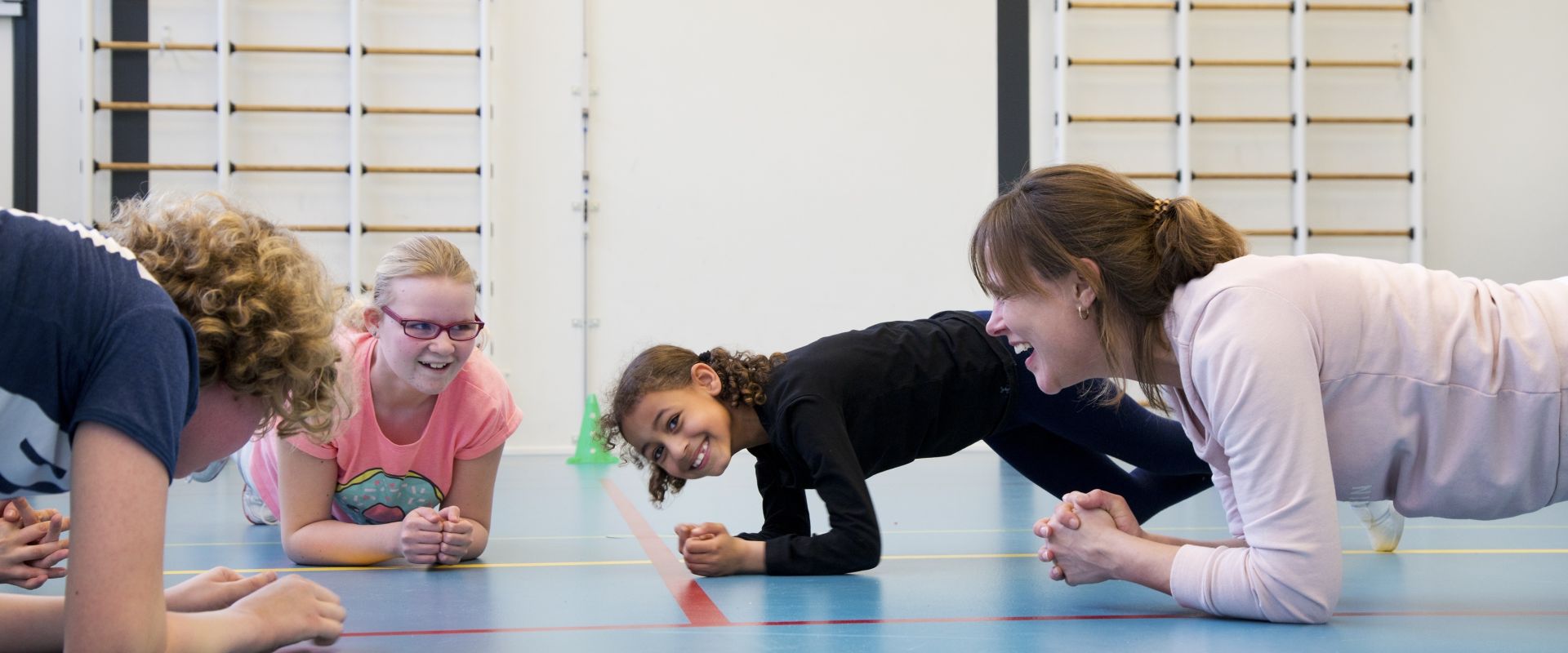 Drie kinderen planken in een gymzaal onder begeleiding van een zorgprofessional