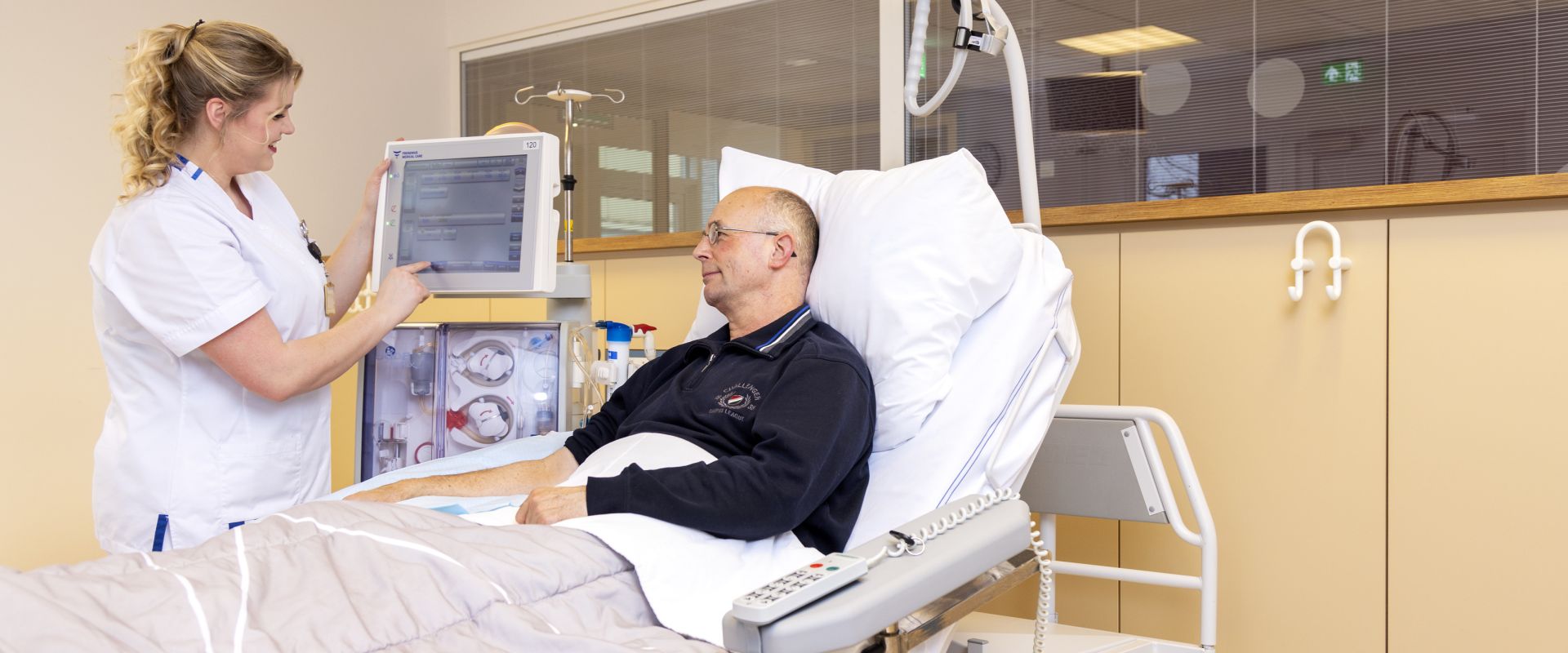 Man in bed, verpleegkundige laat hem iets zien op beeldscherm