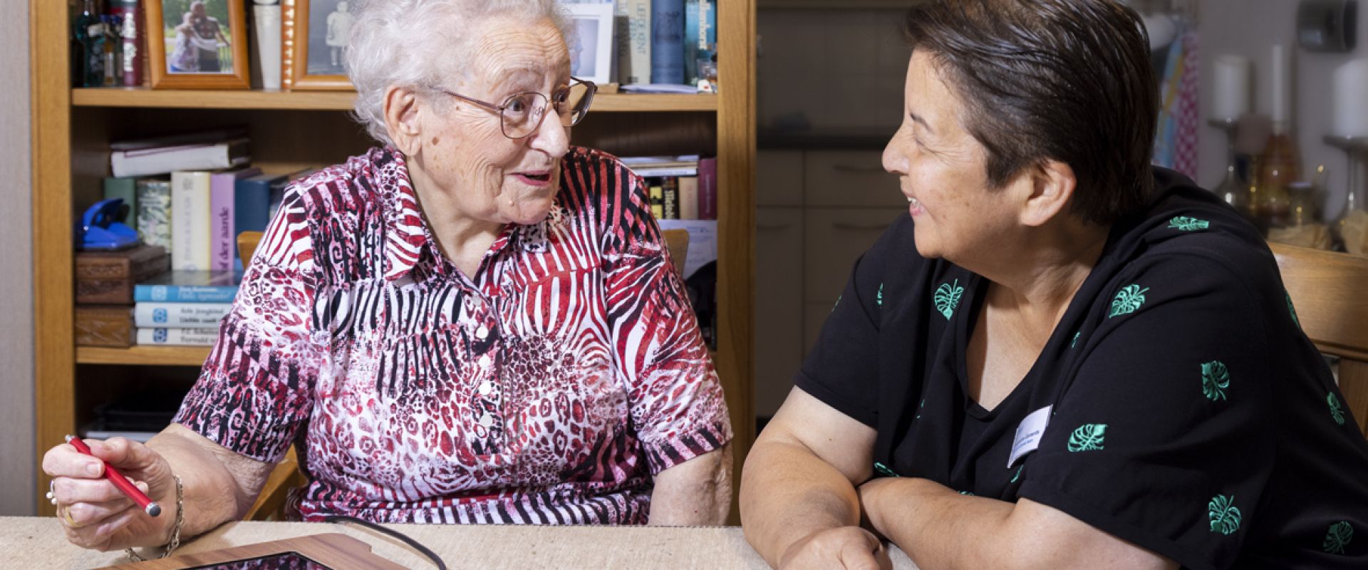 Bewoner is onder begeleiding van een medewerker bezig op haar tablet.
