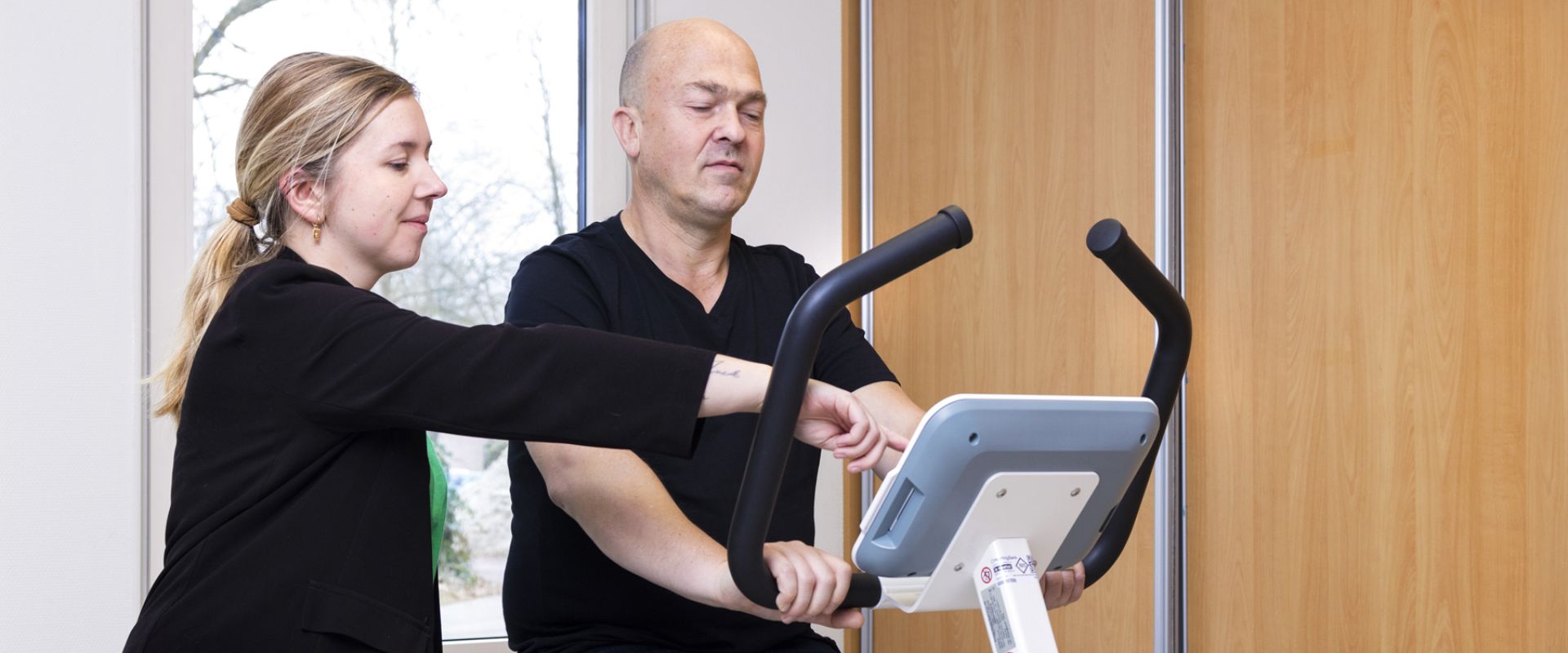 Fysiotherapeut begeleidt meneer op hometrainer