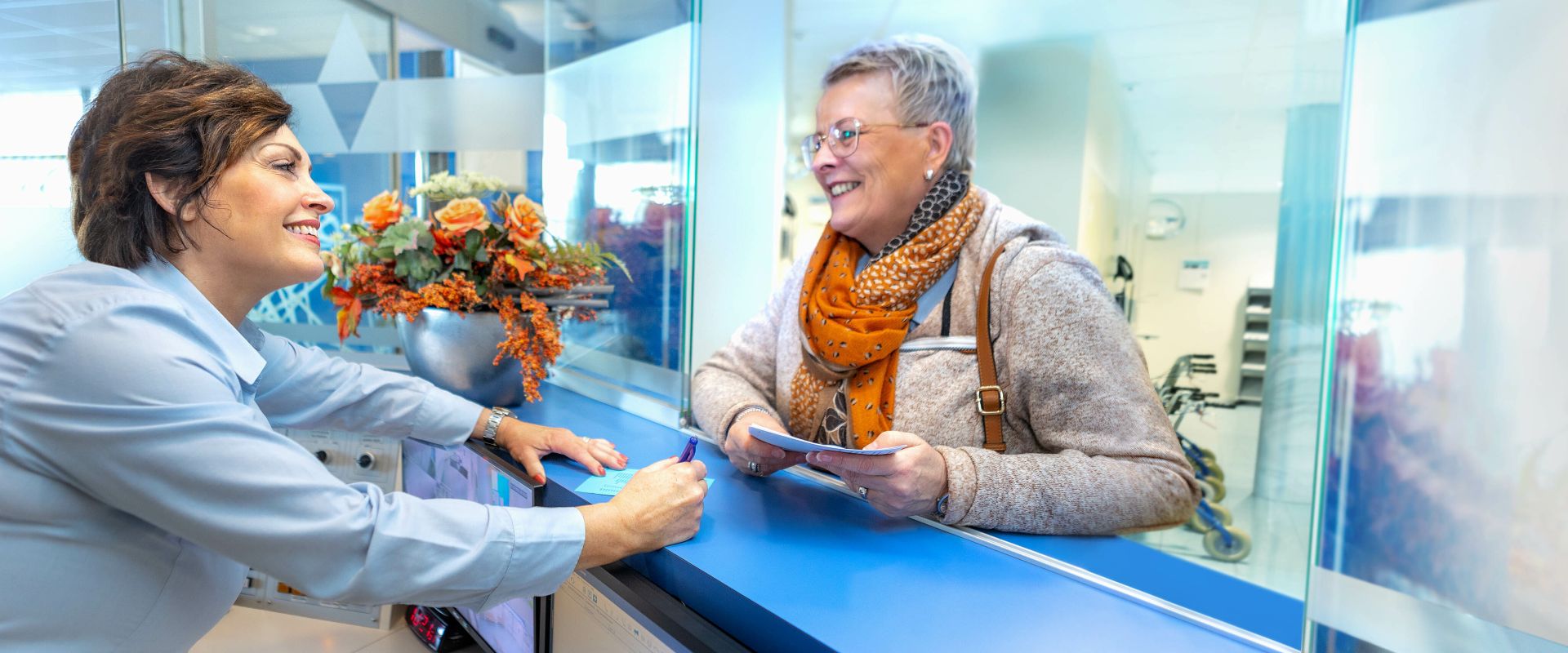 De receptioniste van ziekenhuislocatie Refaja praat met iemand aan de balie.