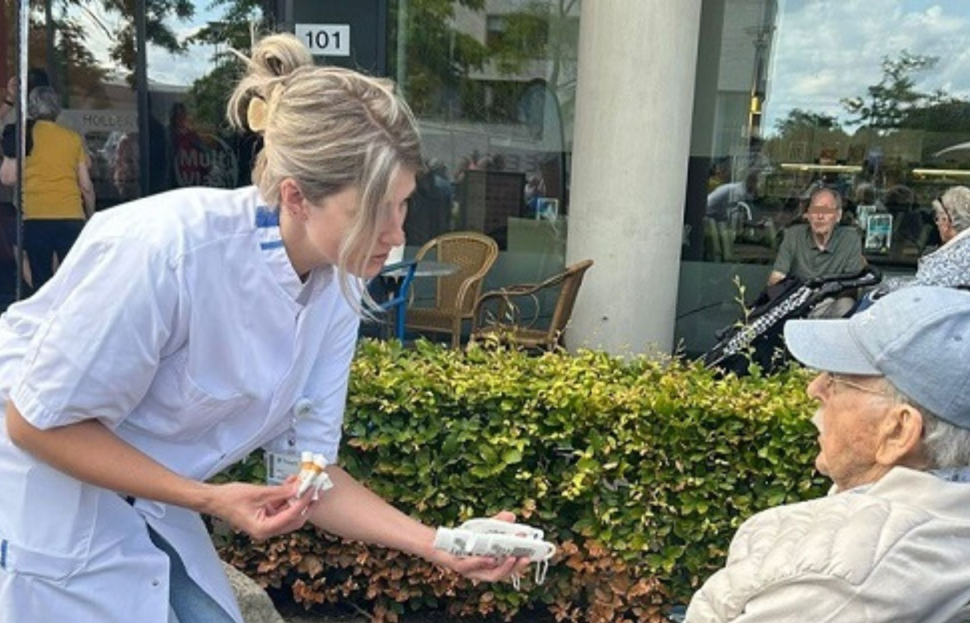 Lorena Tieben deelt zonnebrandcreme uit aan een meneer in een rolstoel tijdens de wandel2daagse van woonzorgcentrum Holdert van Treant