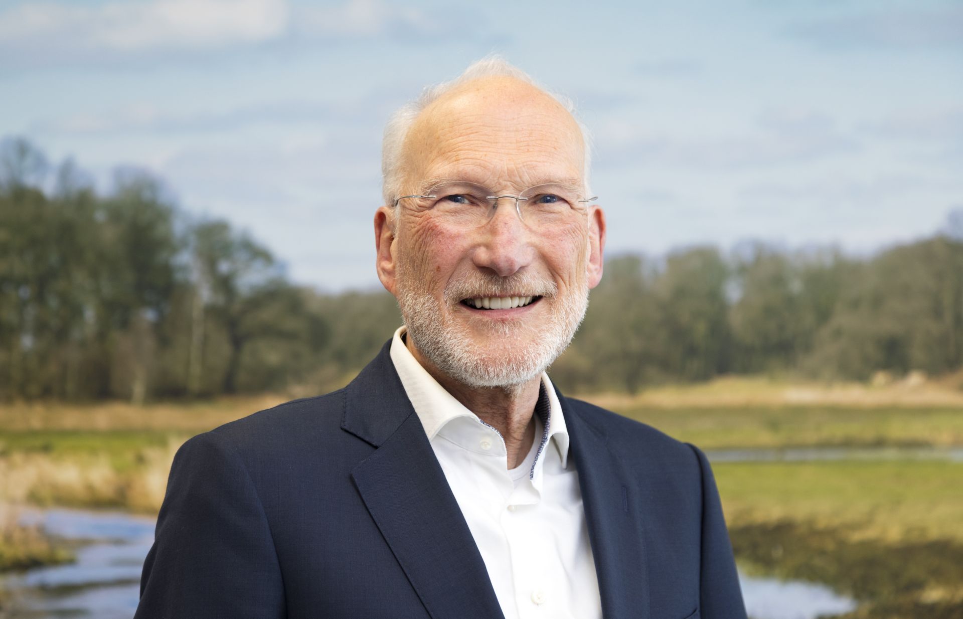 Een oudere man in een pak met een natuurlijke achtergrond.