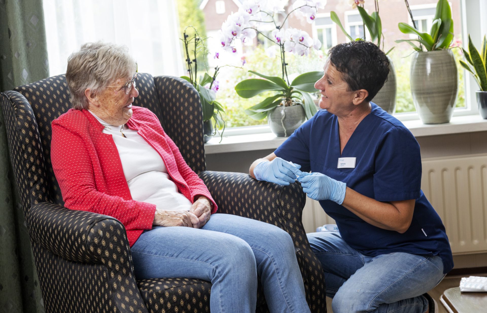 Zorgmedewerker gehurkt bij mevrouw in stoel
