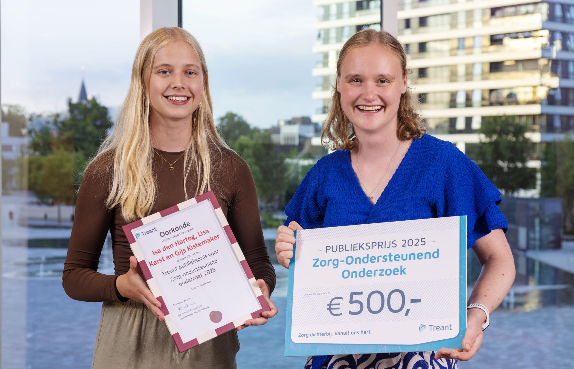 Twee jonge vrouwen poseren met certificaten en een cheque van €500.