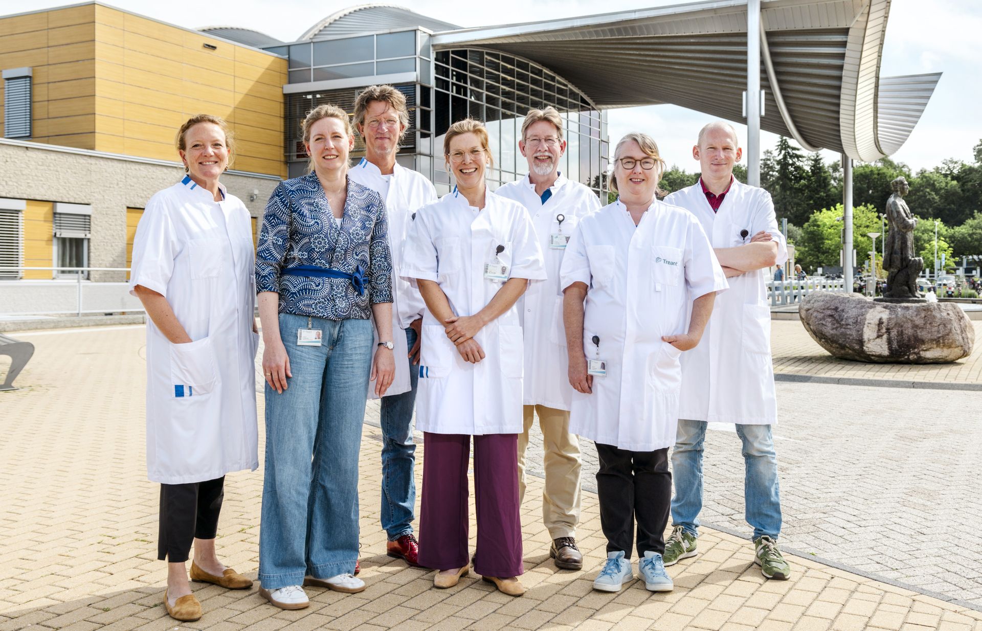 Groep medisch personeel poseert buiten bij een ziekenhuis.