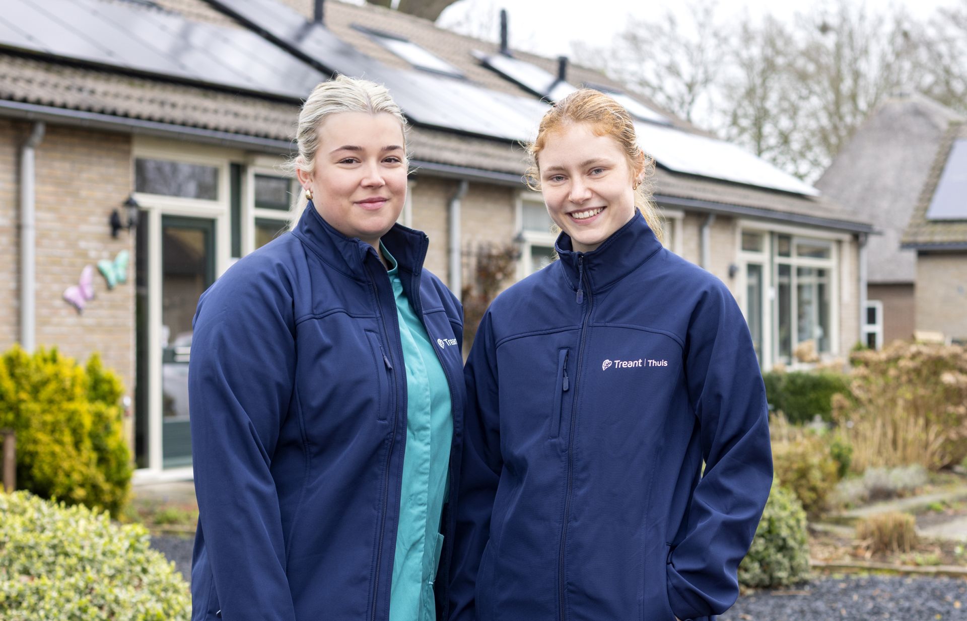 Twee personen in werkkleding van Treant Thuis staan buiten voor een woningen.