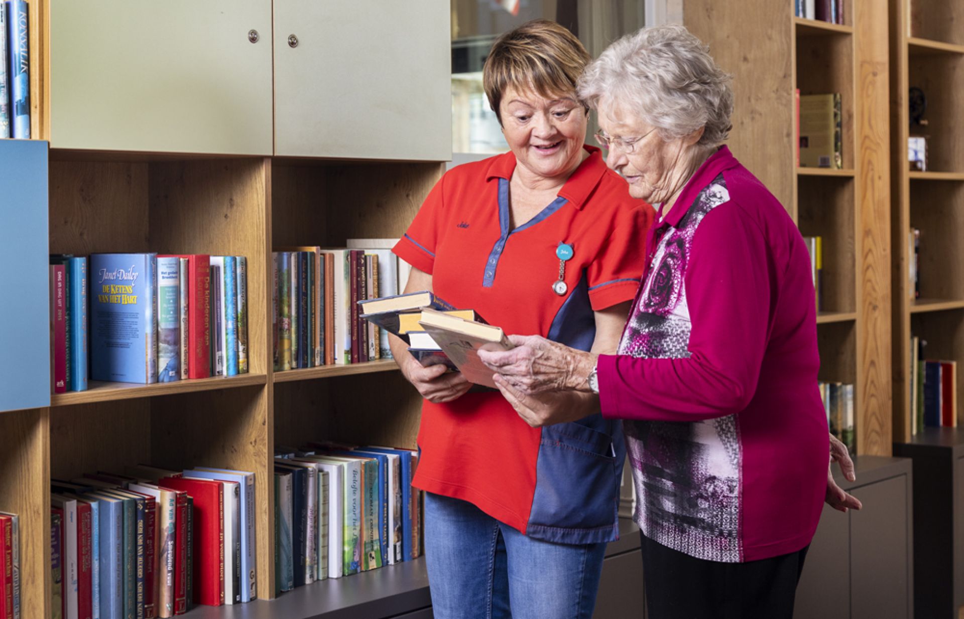 Een medewerkster helpt een bewoonster een boek uit te kiezen