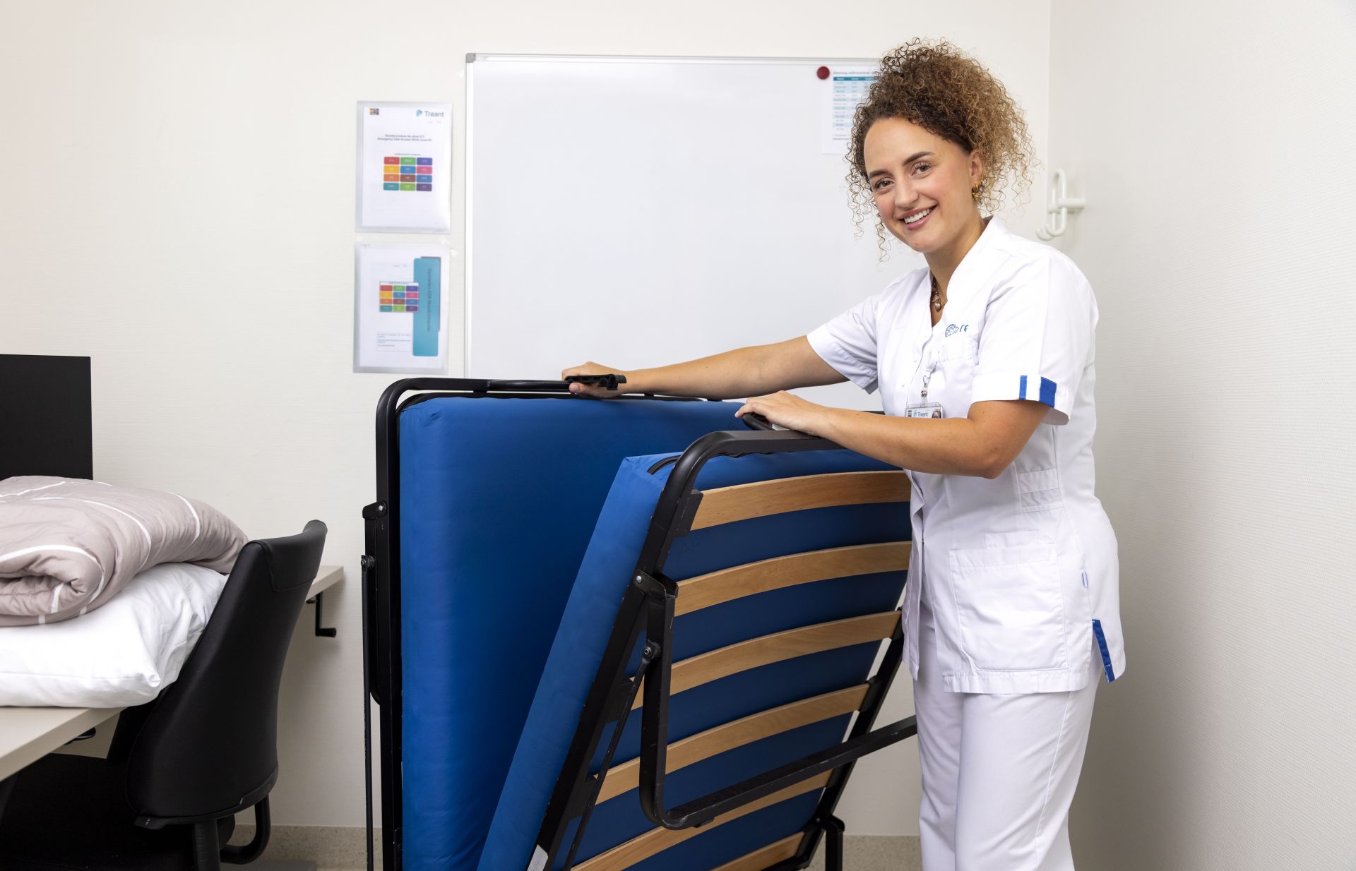 Vrouw in uniform vouwt een bed op in een kantoorruimte.