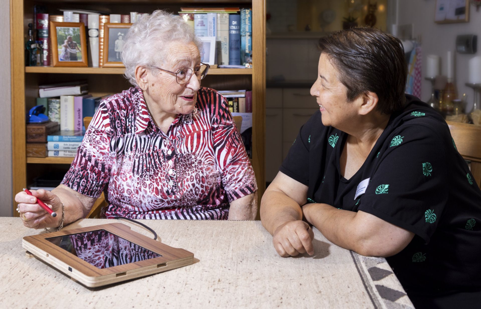 Bewoner is onder begeleiding van een medewerker bezig op haar tablet.