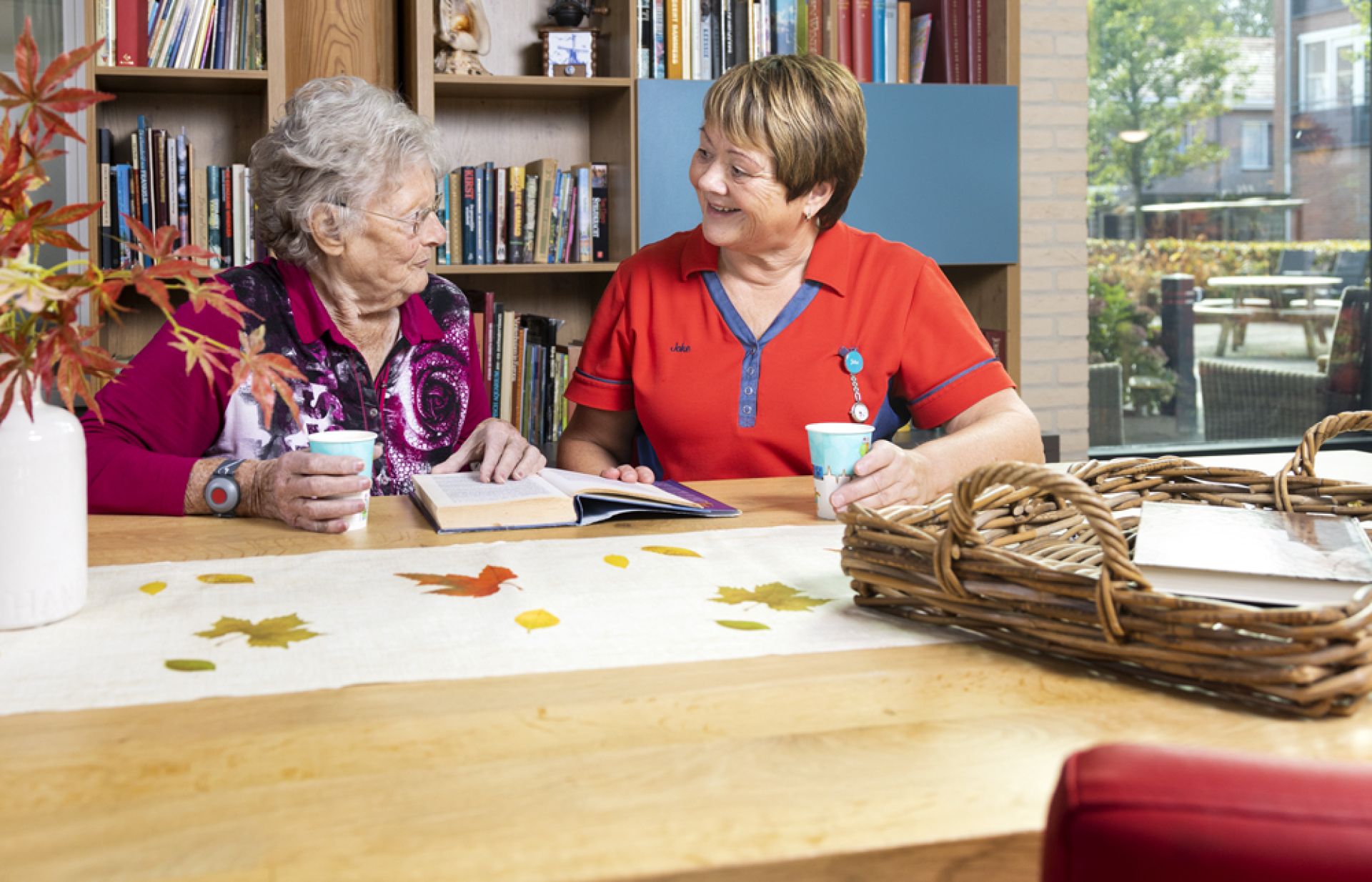 Een bewoonster en medewerker zitten gezellig samen aan tafel.