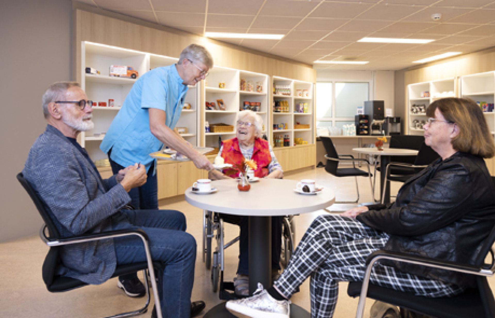 Medewerker van Weidesteyn voorziet aan tafel zittende cliënten van koffie.