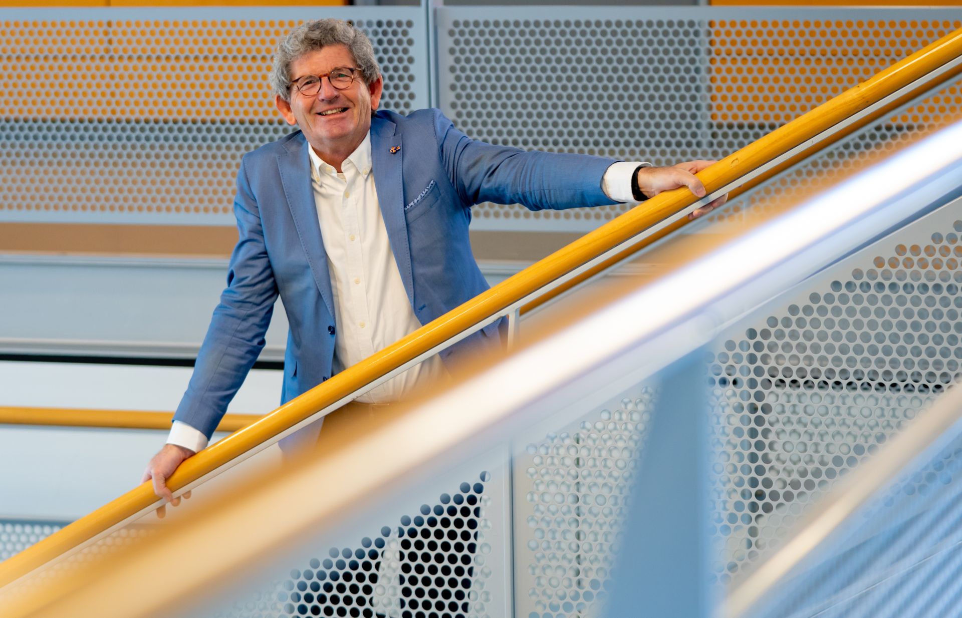 Man leunend op een gele reling in een moderne kantooromgeving.