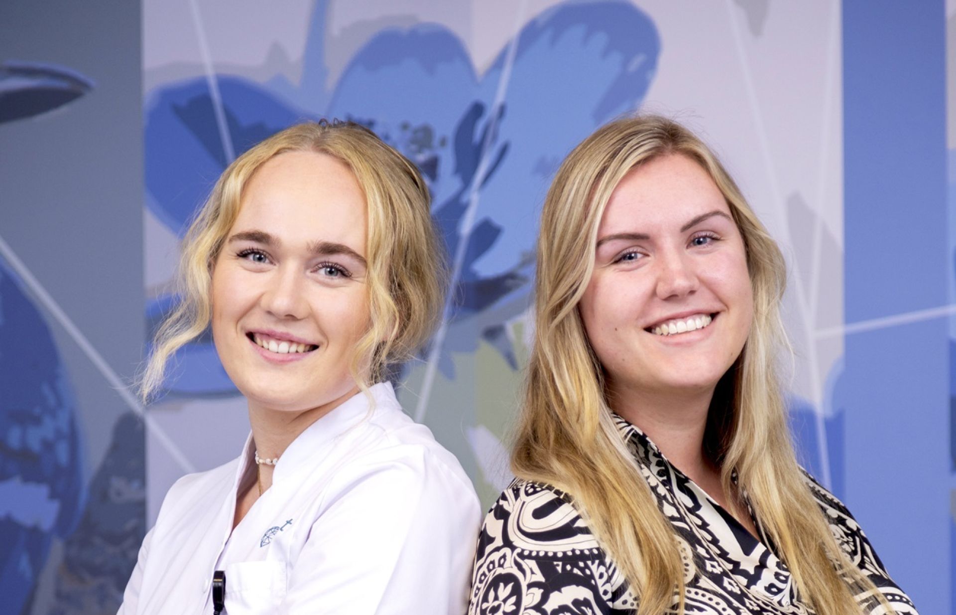 verpleegkundigen Ilse en Sanne die met de ruggen tegen elkaar aan staan en in de camera kijken