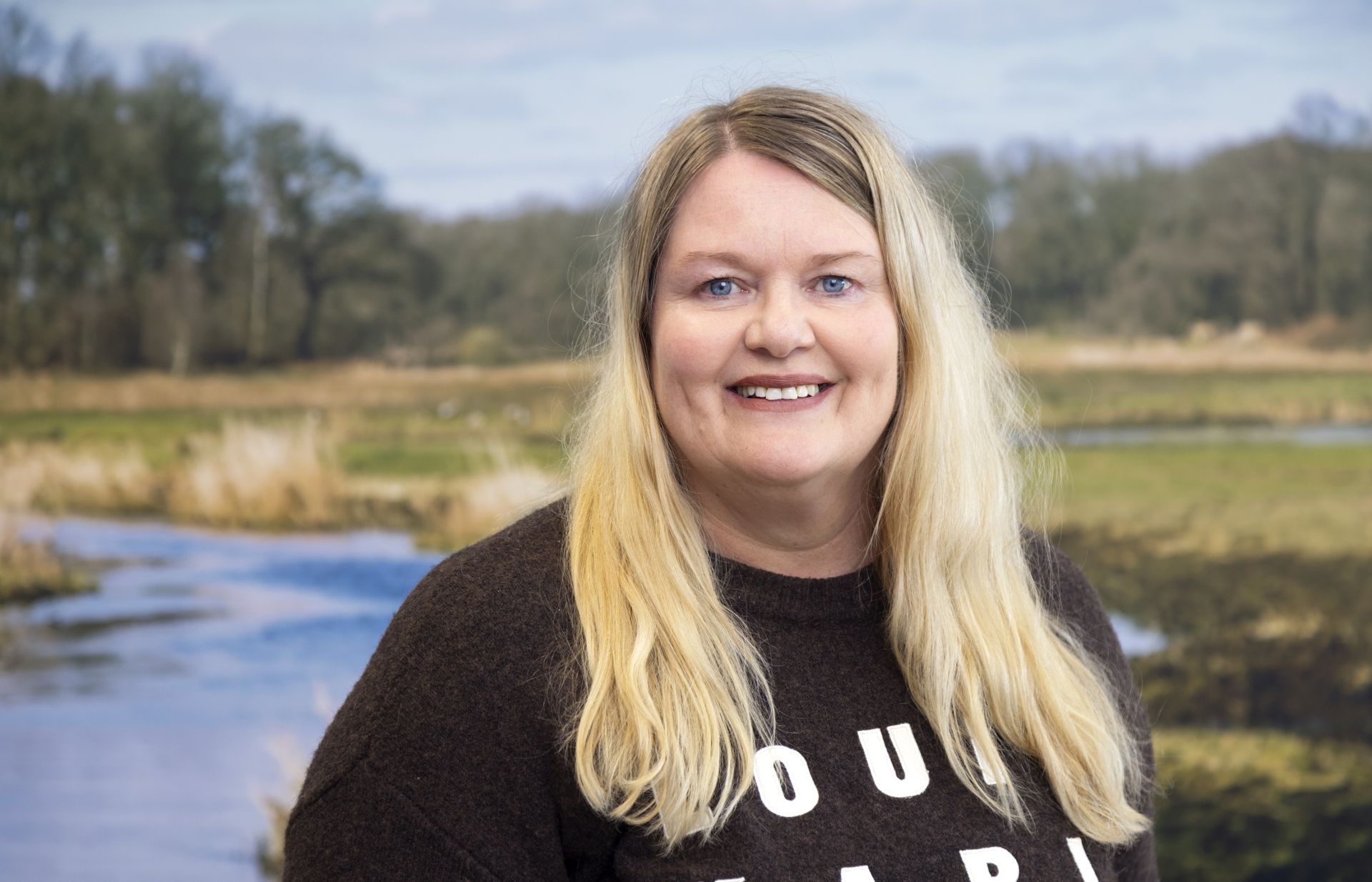 Vrouw met blonde haren staat voor poster met landschap