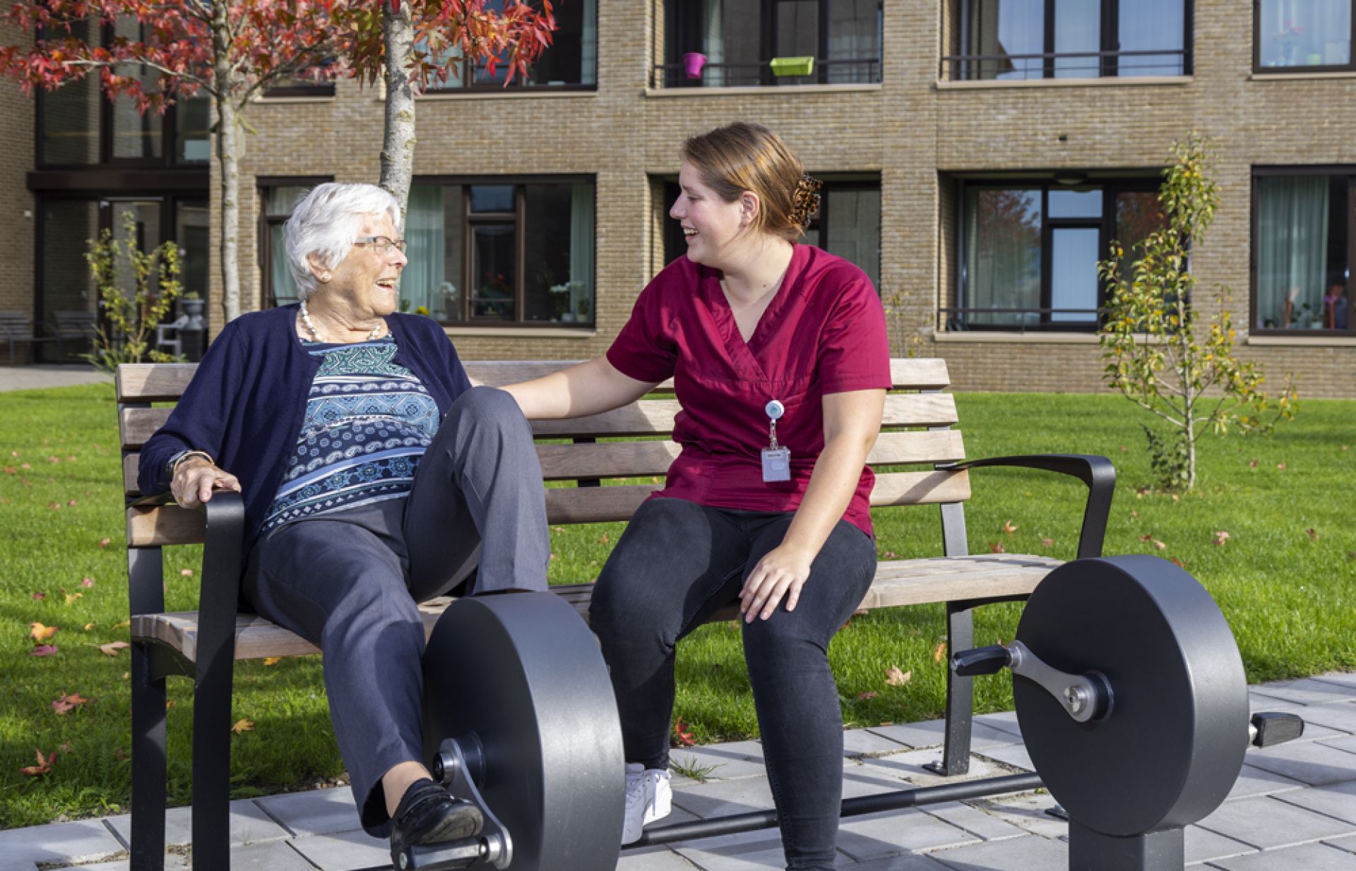 Medewerker en bewoner van Bilderdijk zitten buiten op beweegapparaat