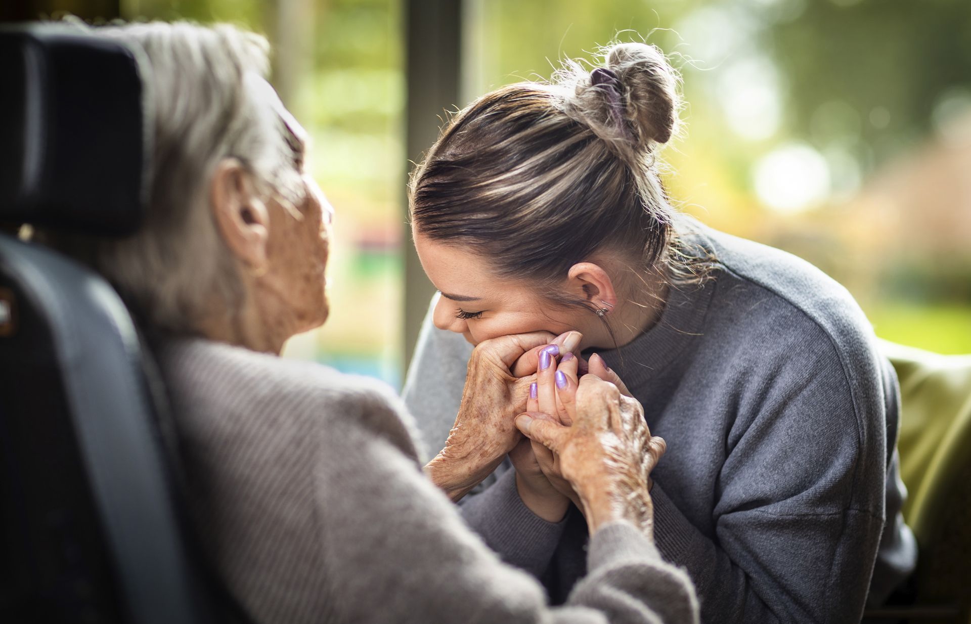 Vrouw houdt handen van oudere vrouw liefhebbend tegen haar gezicht