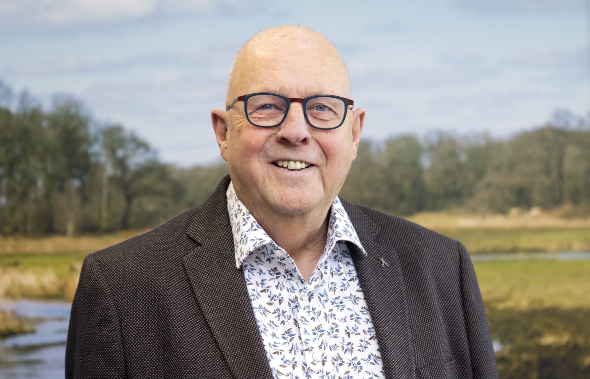 Man met bril poseert voor poster met natuurlandschap.