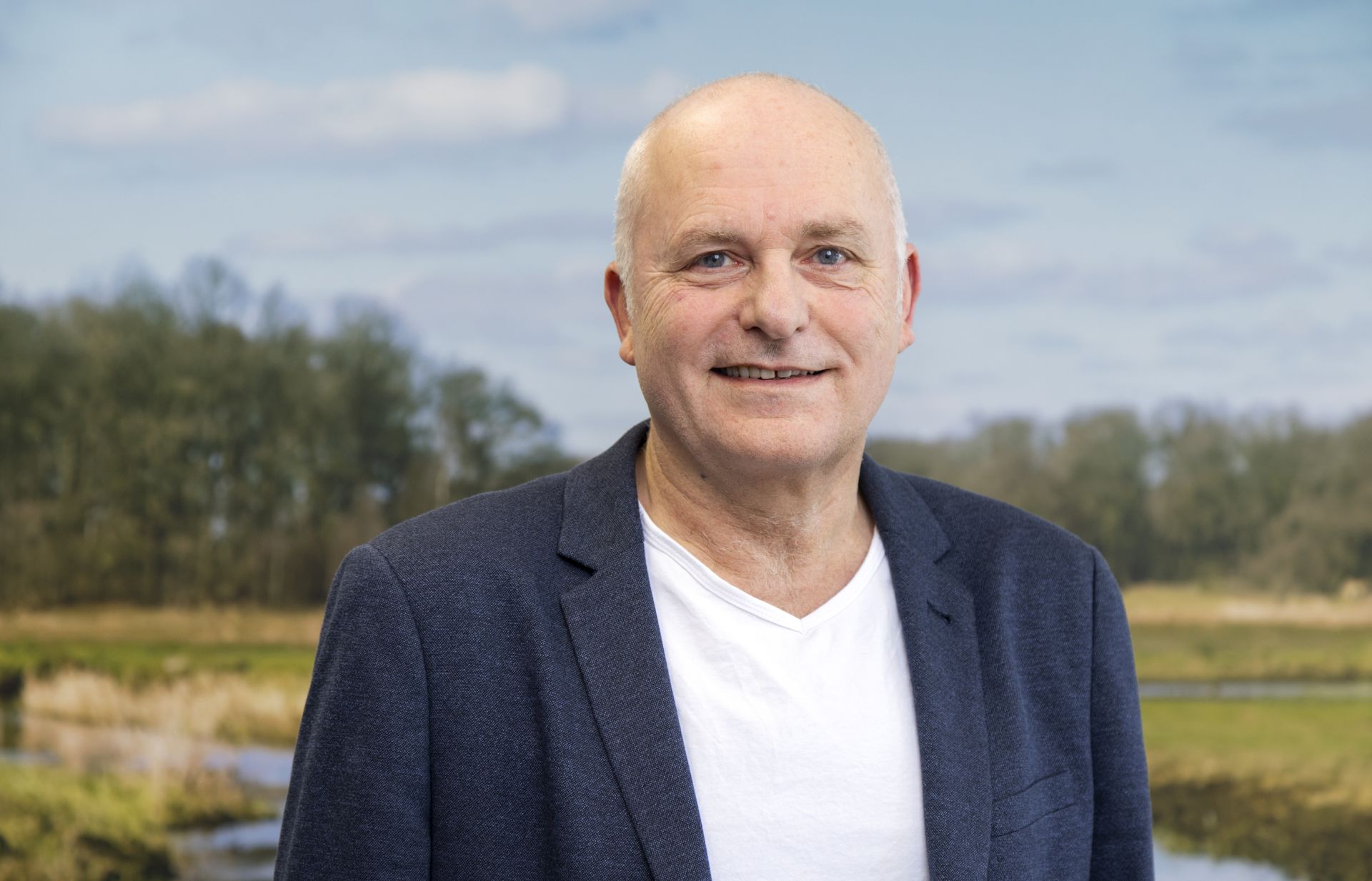 Een man poseert voor een poster met een natuurgebied op de achtergrond.