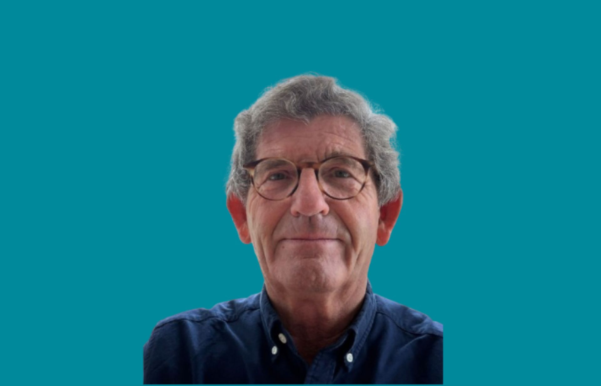 Een oudere man met bril en blauwe trui tegen een turquoise achtergrond.