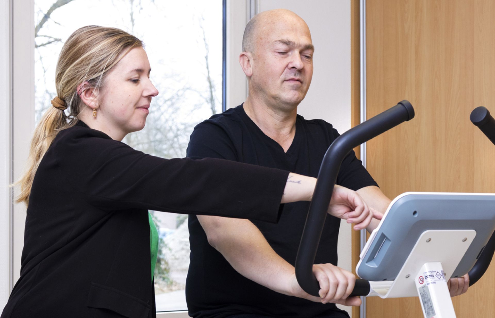 Fysiotherapeut begeleidt meneer op hometrainer