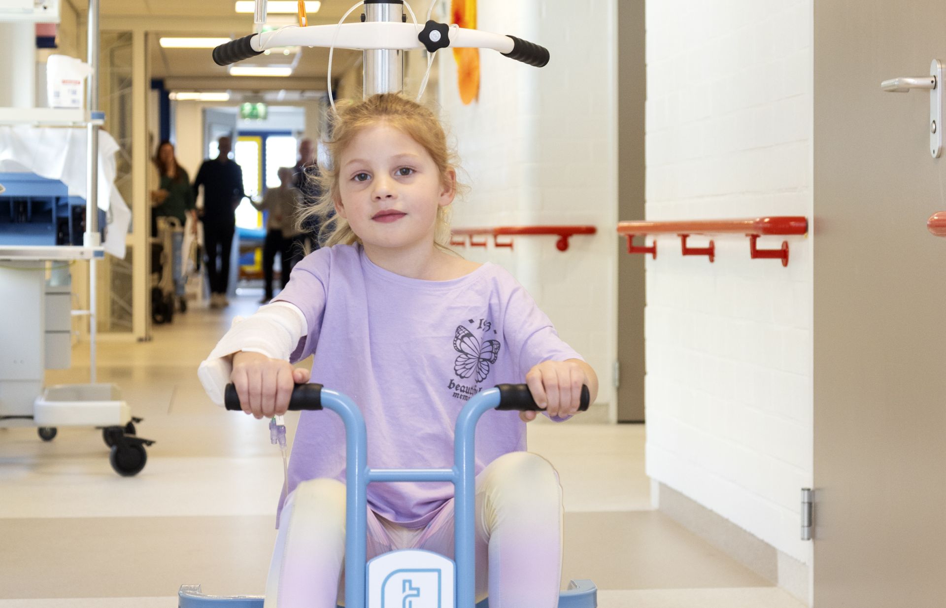 Een jong meisje rijdt op een driewieler door de ziekenhuishal.