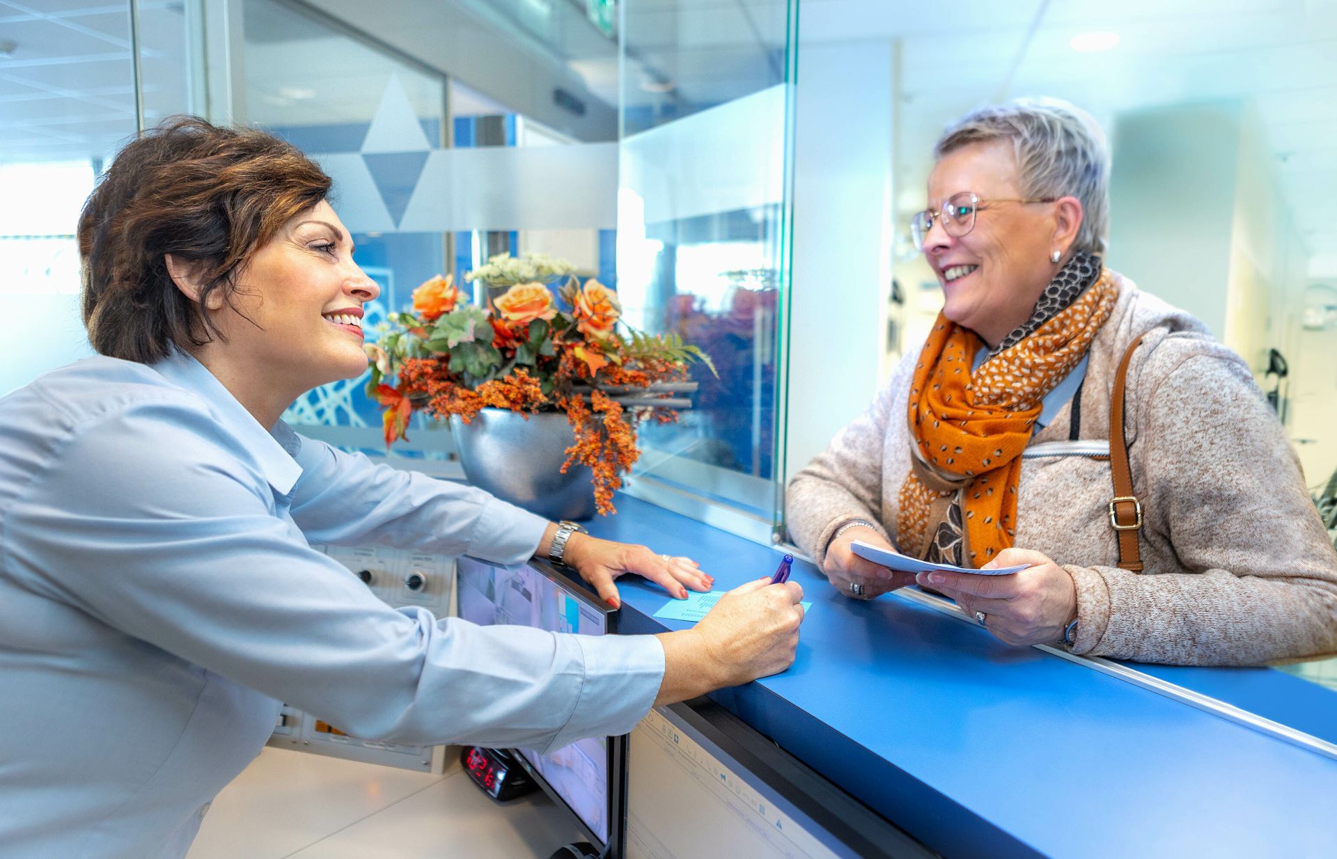 De receptioniste van ziekenhuislocatie Refaja praat met iemand aan de balie.