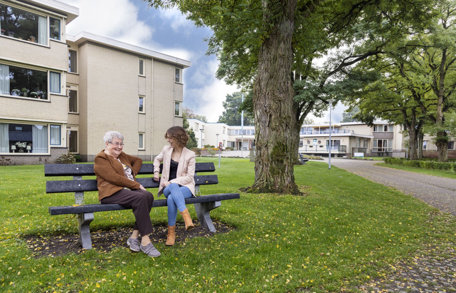 Medewerker en cliënt zitten samen op een bankje voor Het Ellertsveld