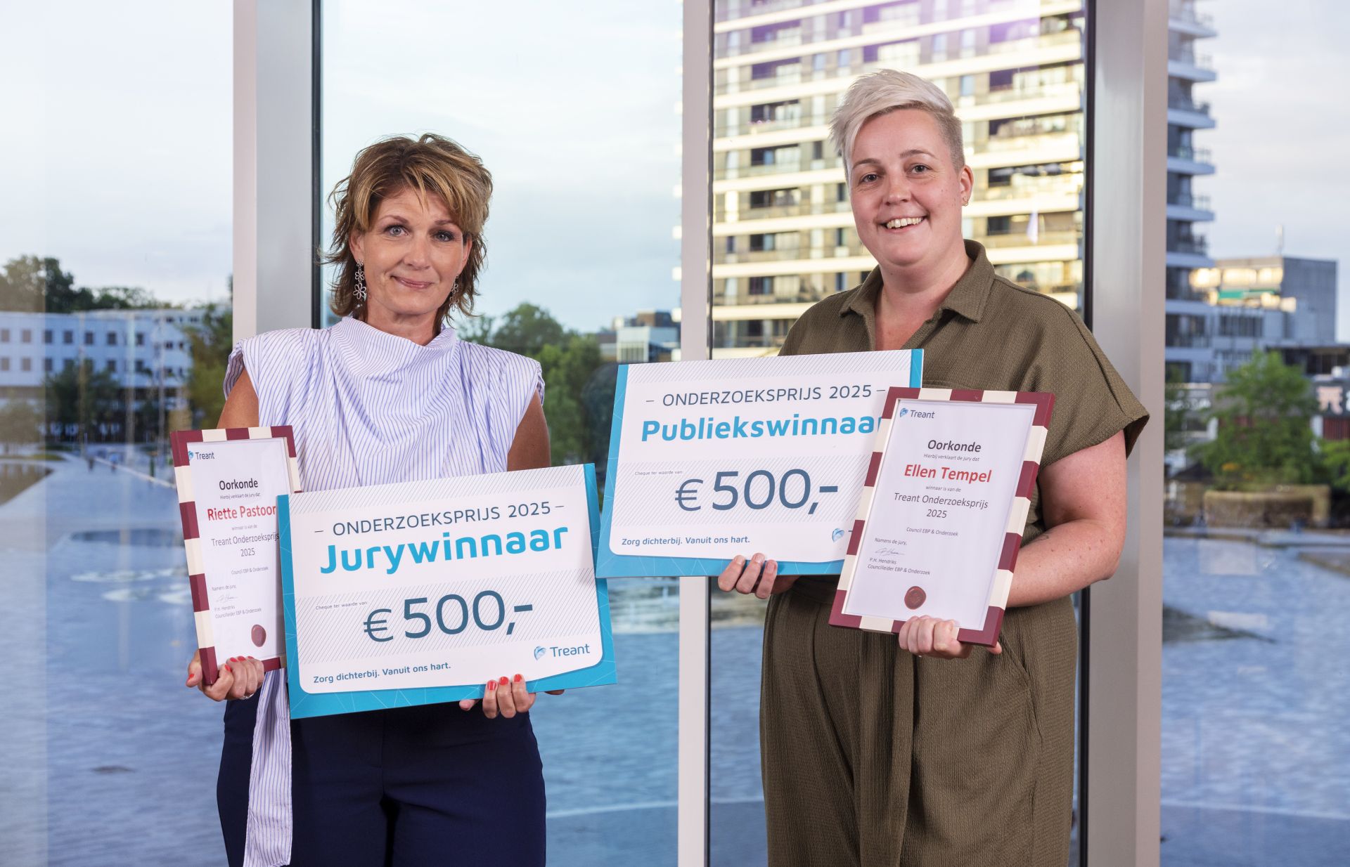 Twee vrouwen met erkenningscertificaten en cheques van €500 voor een prijsuitreiking.
