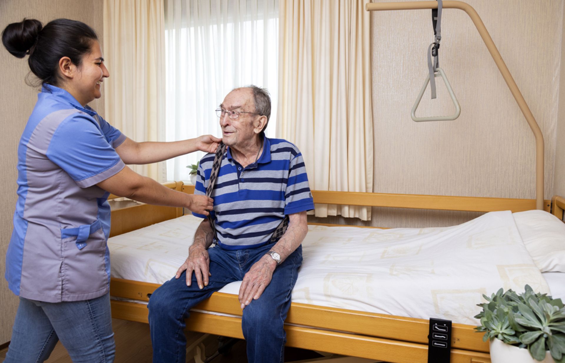 Medewerker helpt cliënt in Valkenhof met het aankleden op zijn bed.
