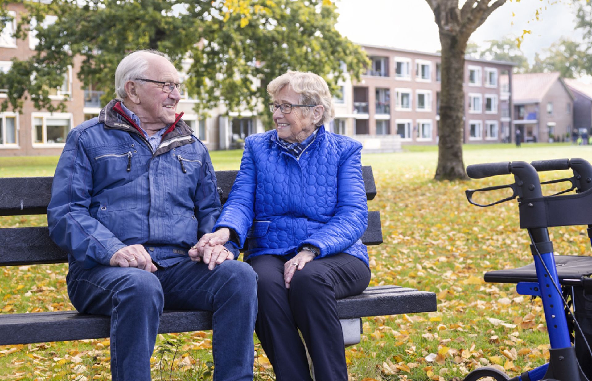 Twee bewoners van De Schutse zitten gezellig samen buiten op een bankje te praten.