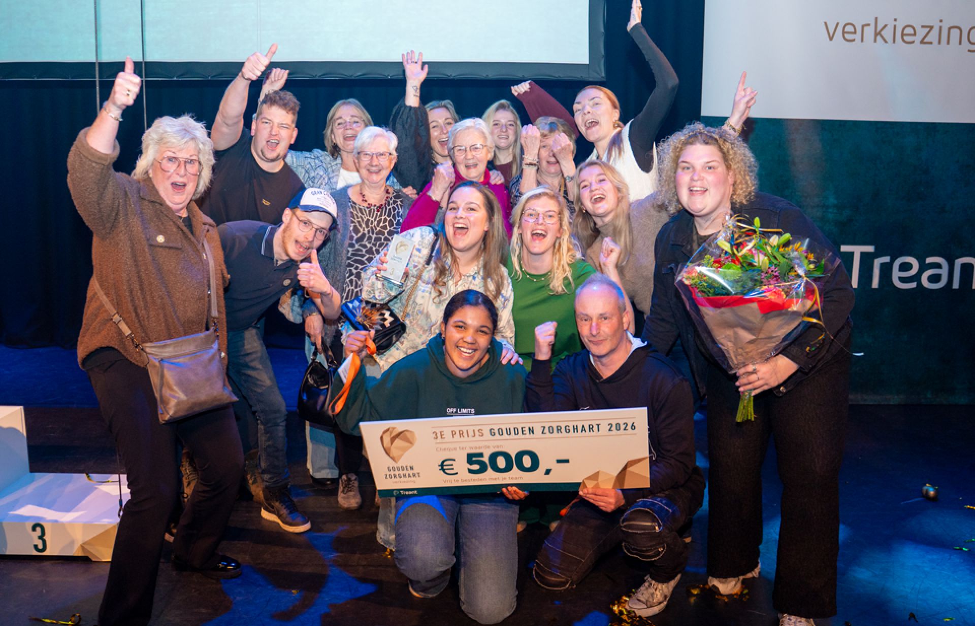 Collega's lachen enthousiat met de cheque van 500 euro in de hand en een bos bloemen