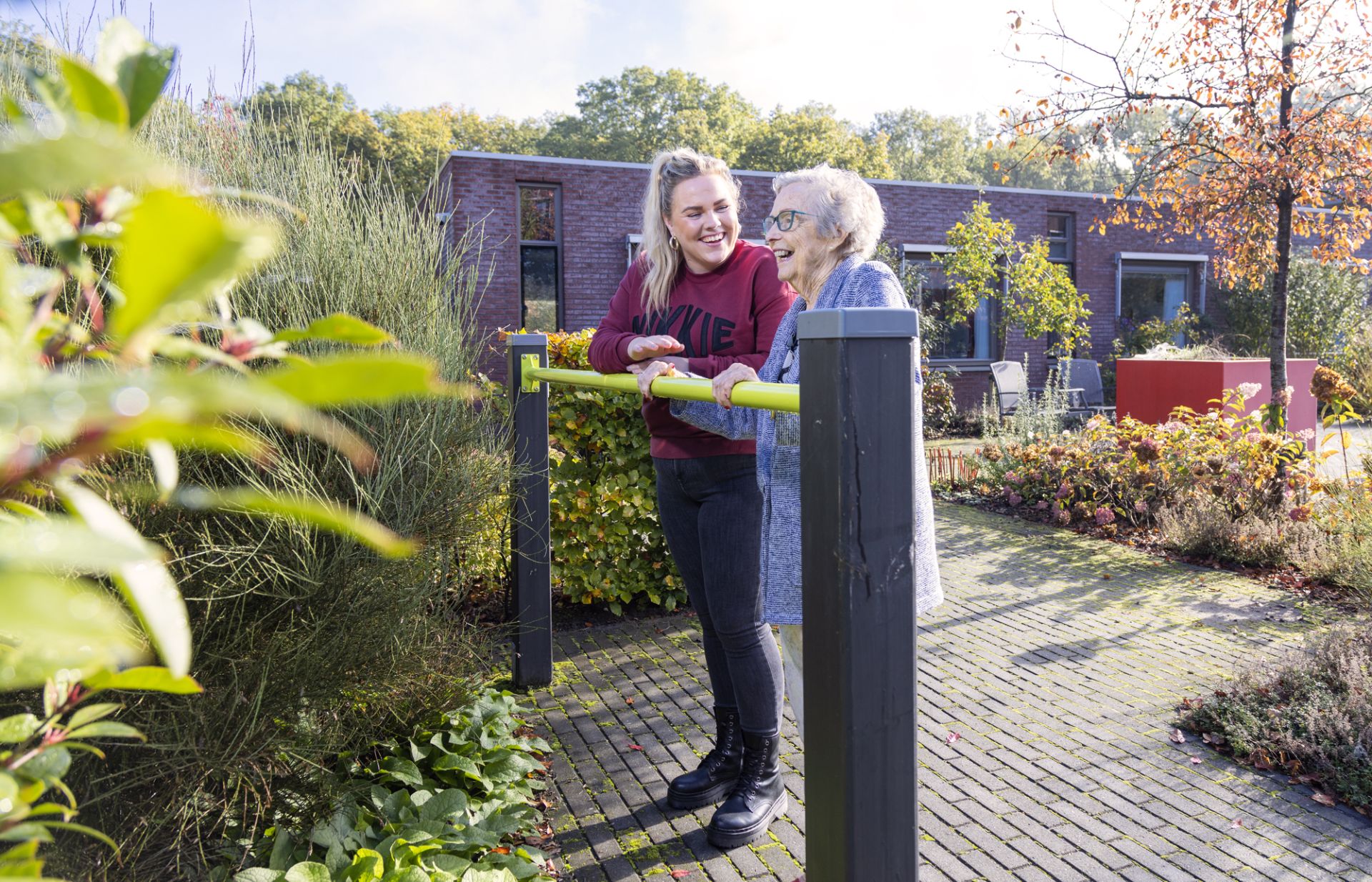 Een medewerker en bewoner van De Paasbergen zijn samen buiten aan het sporten bij een beweegtoestel