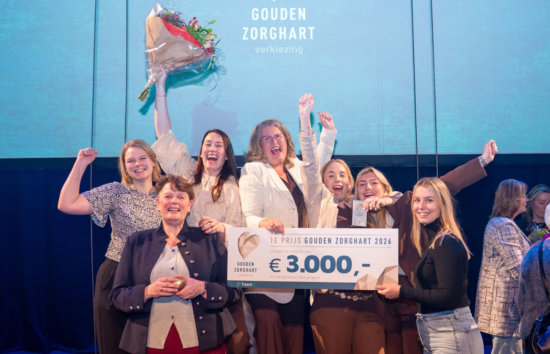 Collega's van woonzorgcentrum Holdert in Emmen juichen enthousiat met de cheque van 3000 euro in de hand en een bos bloemen
