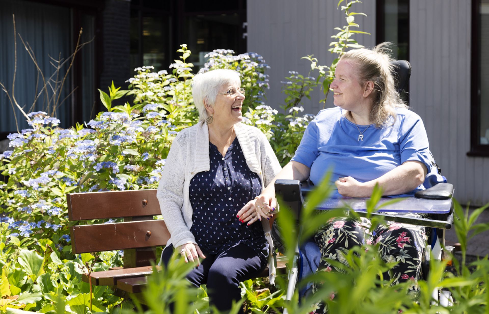 Twee dames zitten buiten op een bankje en hebben plezier in de tuin van De Horst