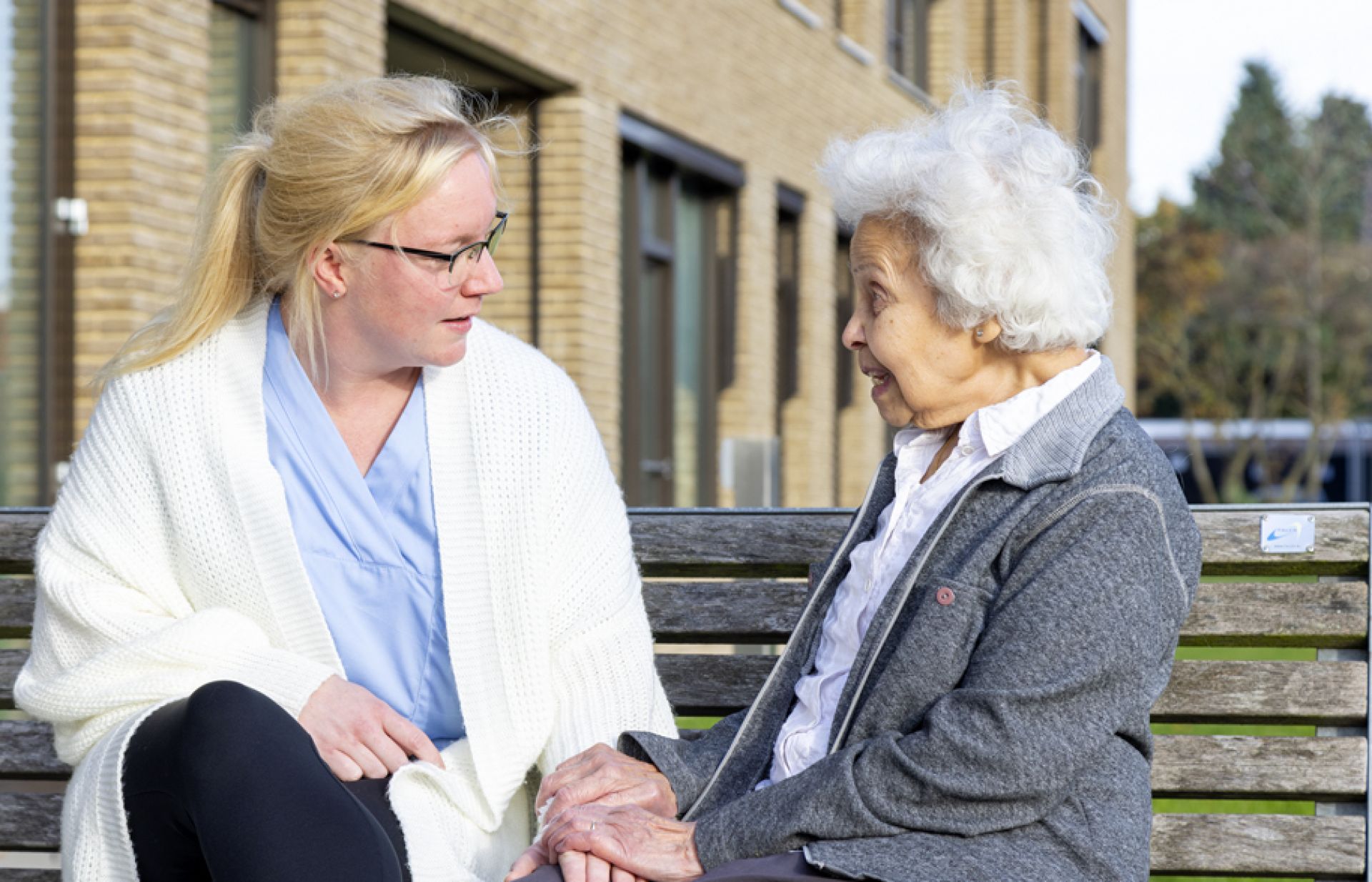 Medewerker en bewoner van Bilderdijk zitten buiten op een bankje