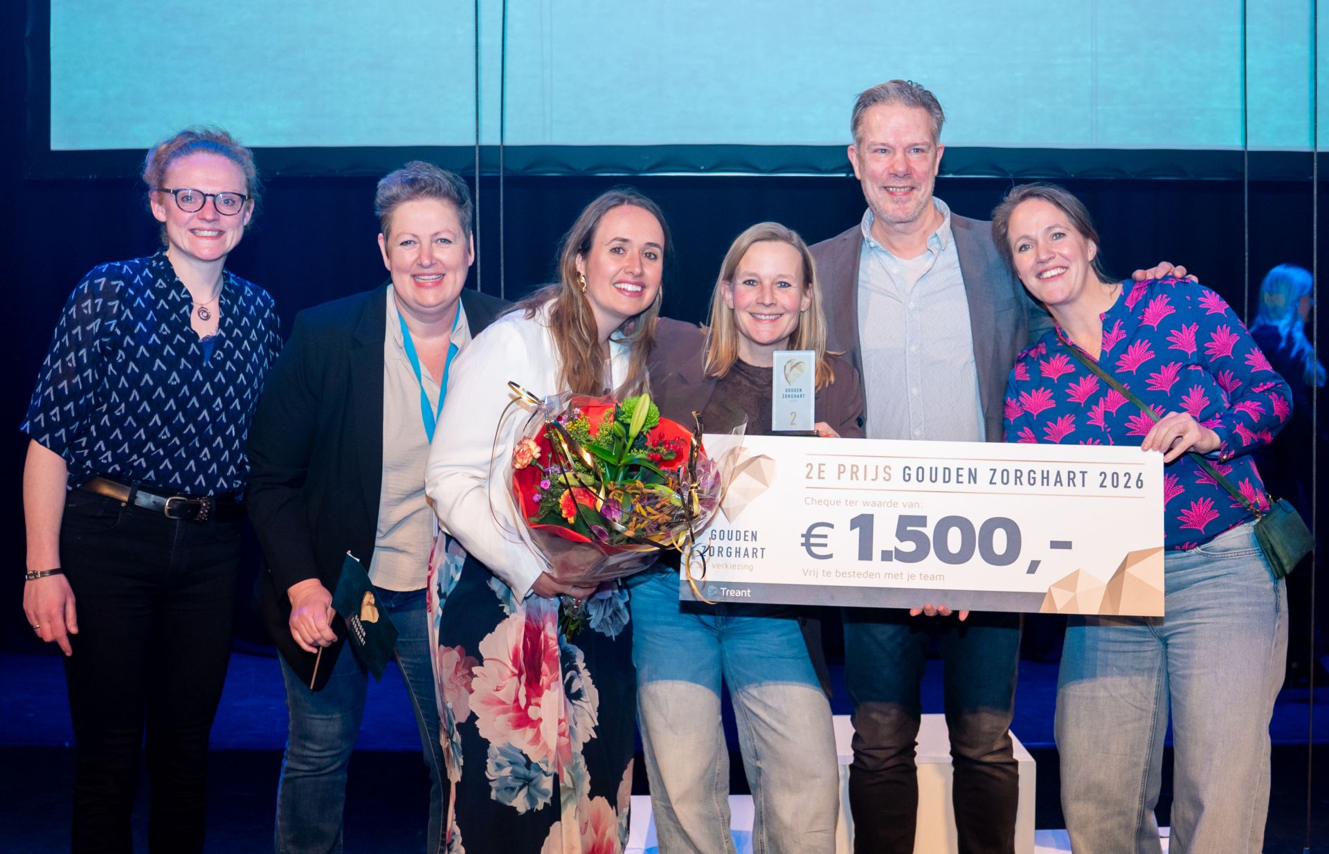 Collega's lachen enthousiat met de cheque van 1500 euro in de hand en een bos bloemen