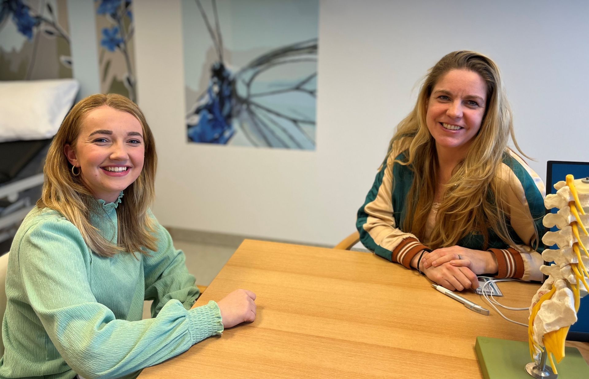 Verpleegkundigen Selina en Wietske zitten in de spreekkamer van Wietske aan tafel.