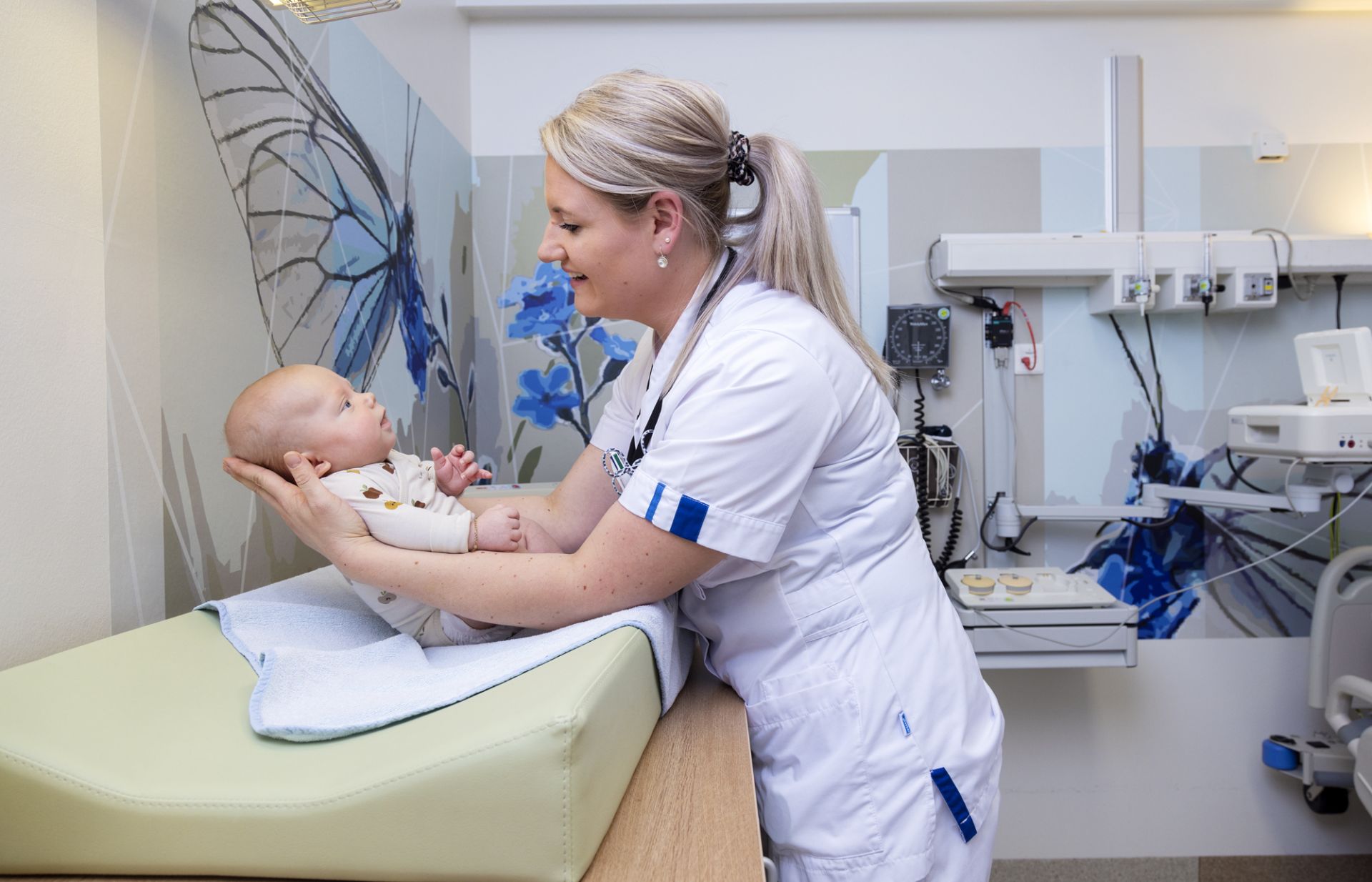 Een zorgmedewerker houdt een baby vast op het aankleedkussen