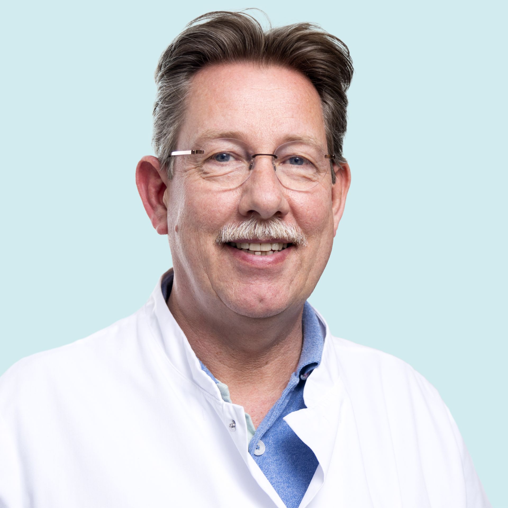 man in een witte doktersjas en met een blauwe blouse.