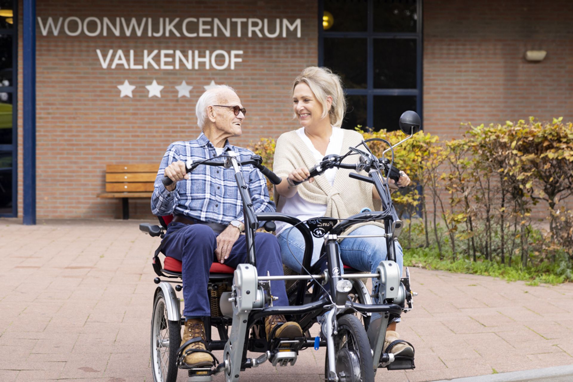 Bewoner Valkenhof zit samen met medewerker op een fiets voor woonwijkcentrum Valkenhof