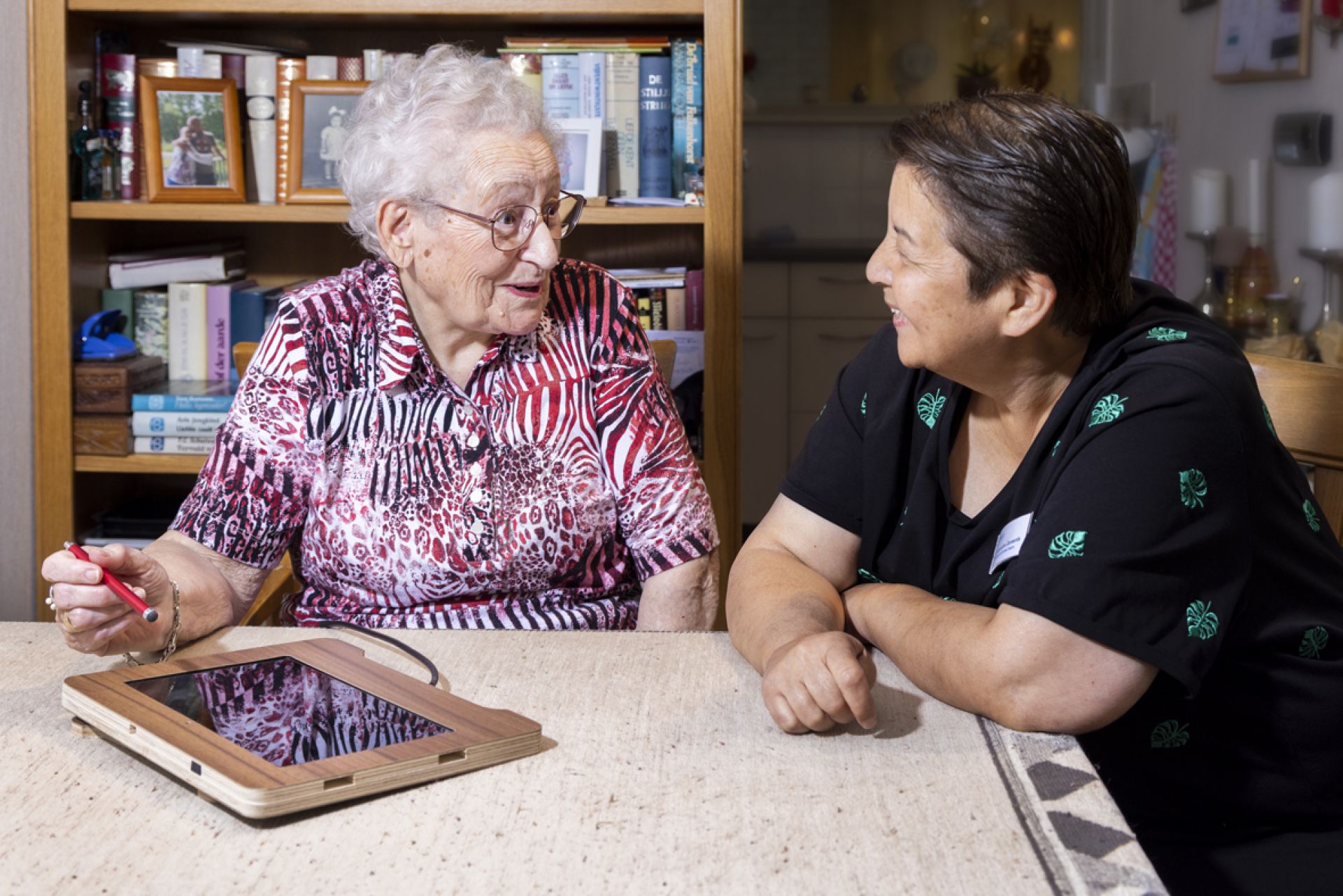 Bewoner is onder begeleiding van een medewerker bezig op haar tablet.