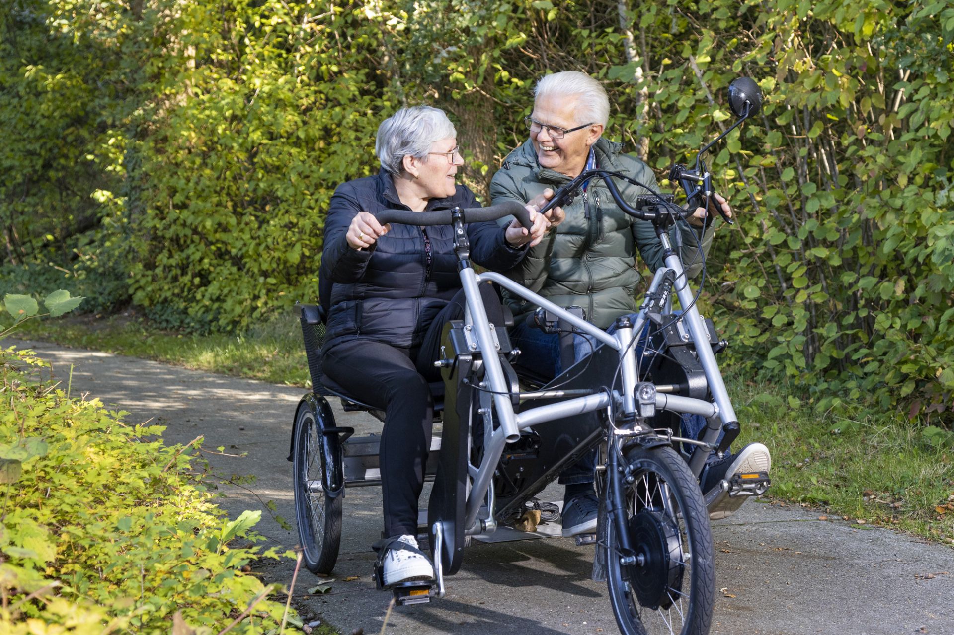 Cliënt en vrijwiller fietsen samen door het bos op een duofiets