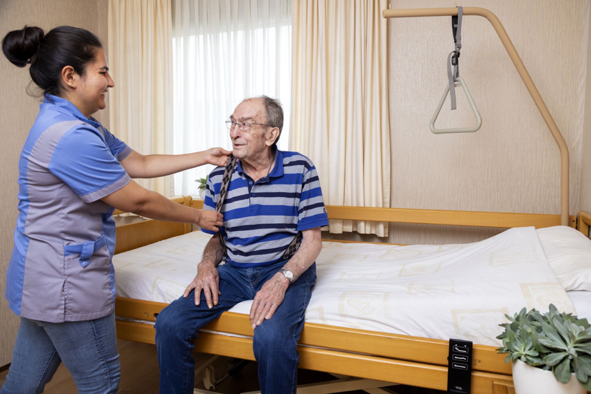 Medewerker helpt cliënt in Valkenhof met het aankleden op zijn bed.