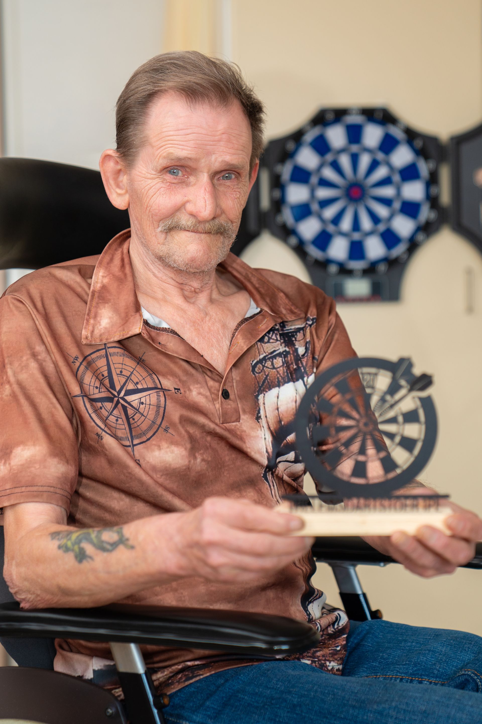 Een man houdt een prijs vast met een dartbord op de achtergrond.