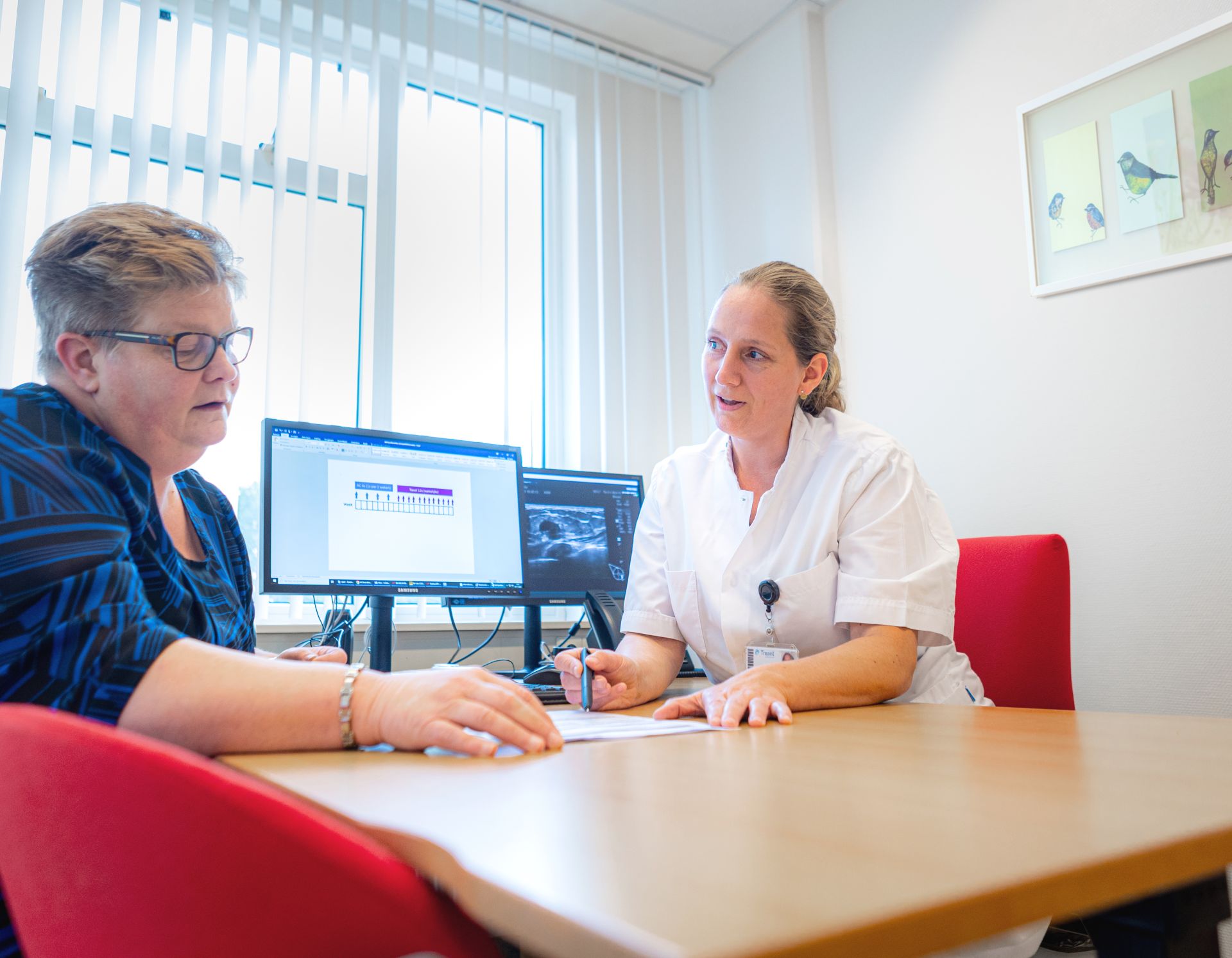 Een arts is in gesprek met een patient. Zittend aan een tafel.