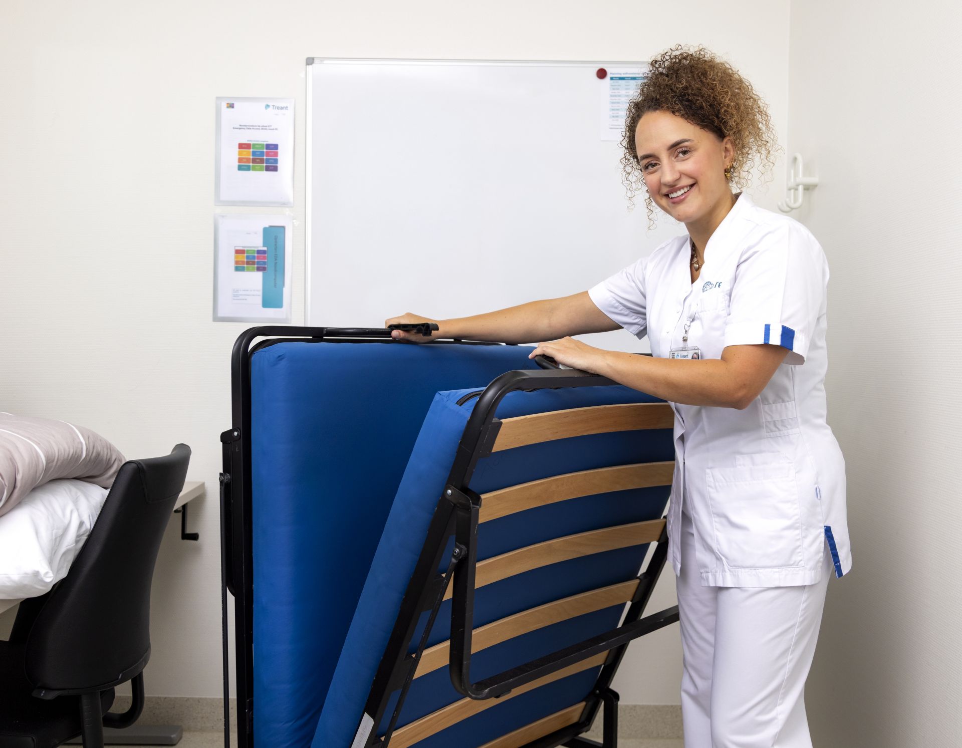 Vrouw in uniform vouwt een bed op in een kantoorruimte.