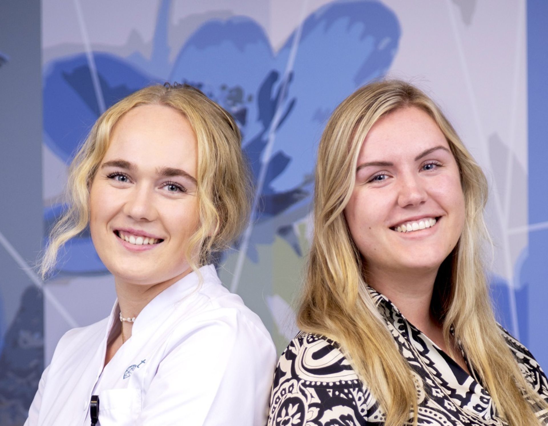 verpleegkundigen Ilse en Sanne die met de ruggen tegen elkaar aan staan en in de camera kijken