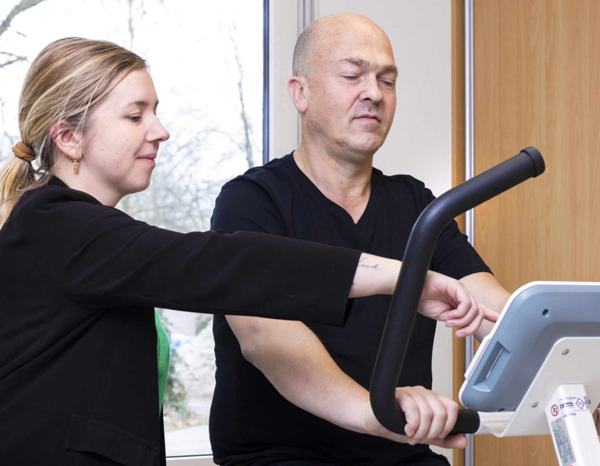 Fysiotherapeut begeleidt meneer op hometrainer